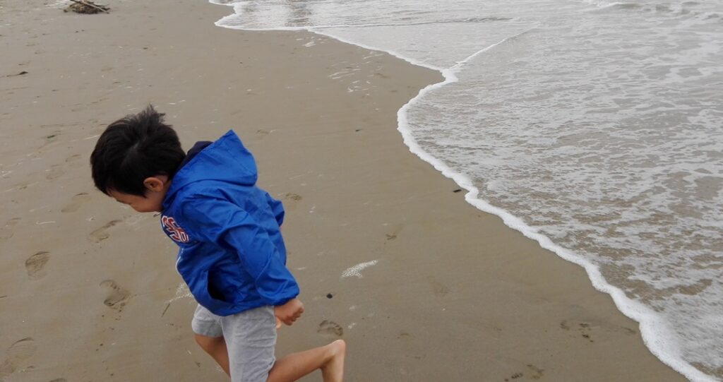 해변 모래사장을 달리는 아이와 잔잔한 파도