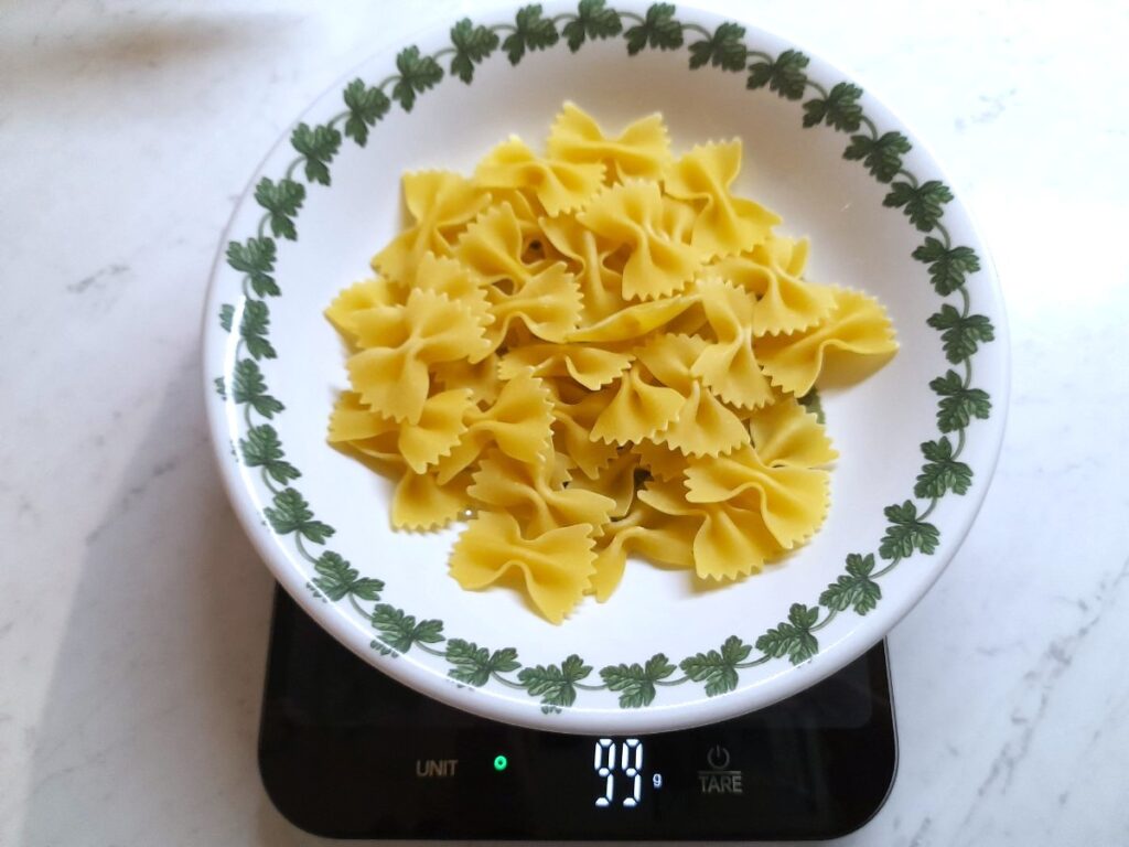 주방 저울 위 접시에 담긴 파르팔레 파스타가 99g으로 표시되어 있다