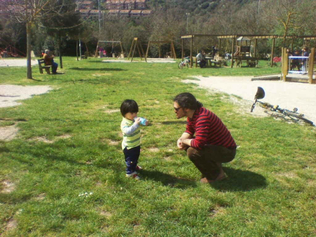물병으로 물을 마시는 어린아이와 아이에게 말을 거는 아빠가 공원의 초록 잔디밭에서 함께 있다