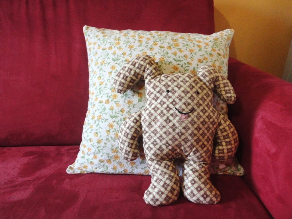 빨간색 소파 위에 노란색 꽃무늬 쿠션 앞에 귀여운 인형이 있다