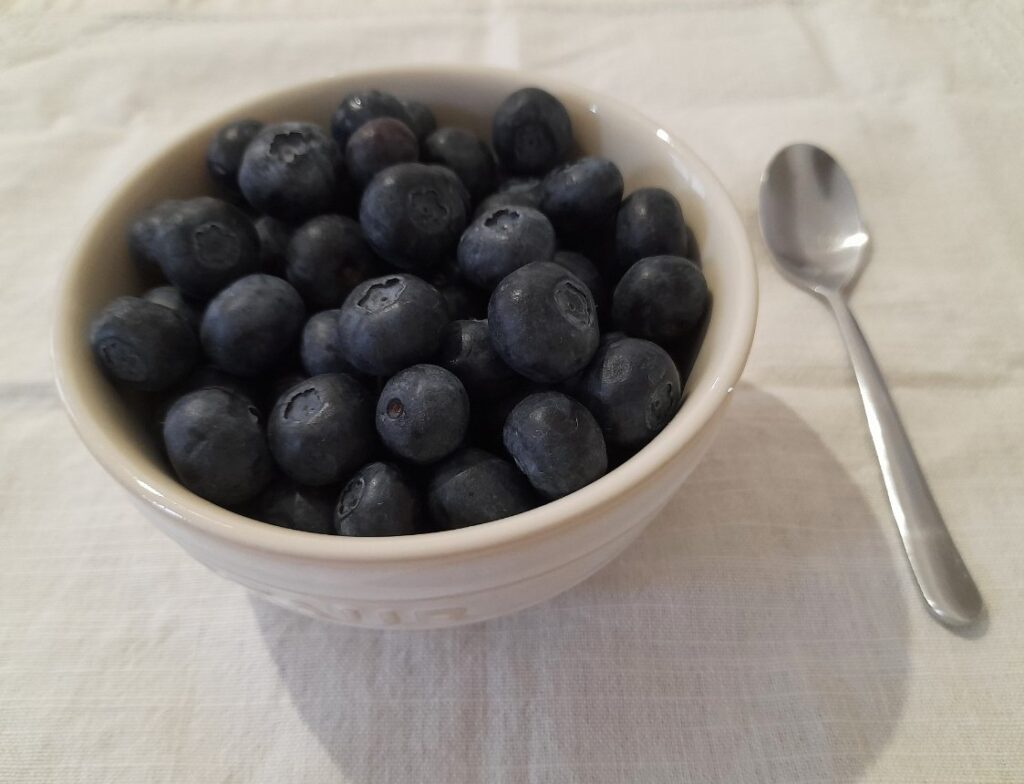 하얀 그릇에 담긴 블루베리와 옆에 놓인 티스푼