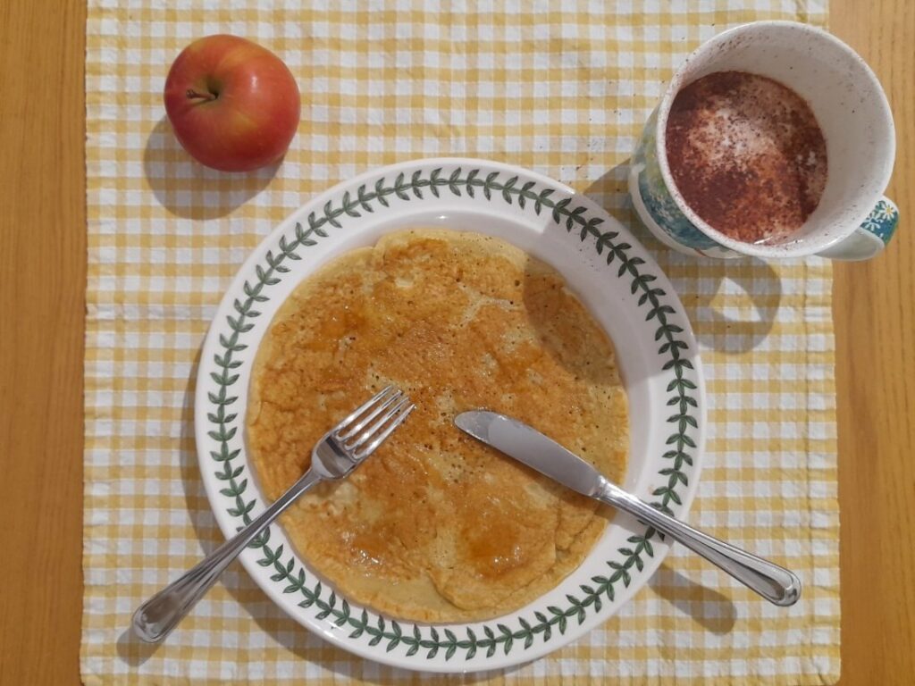 접시에 올린 팬케이크와 사과, 우유가 함께 놓인 아침 식사