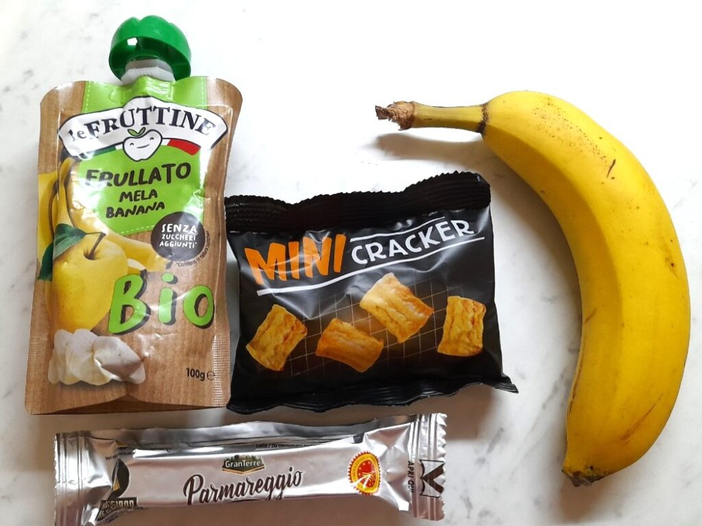 과일 퓨레 파우치와 미니 크래커, 바나나, 치즈 스틱이 함께 놓인 아이 간식 구성