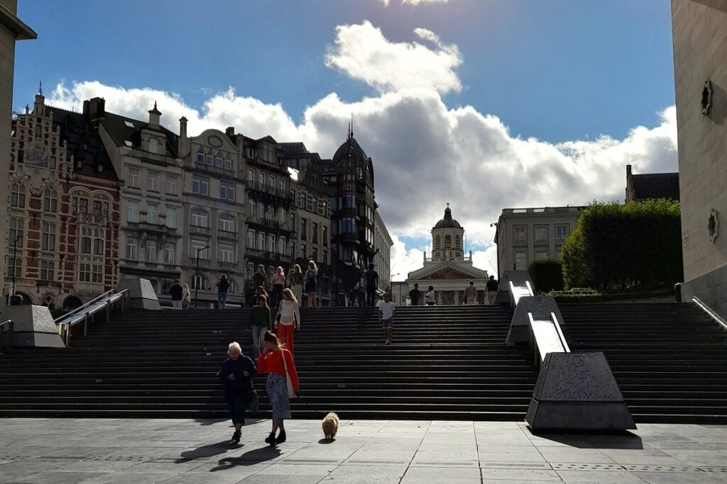 파란 하늘 아래 유럽의 오래된 건물과 계단 앞에서 할머니와 손녀 그리고 강아지가 걷는 거리 풍경