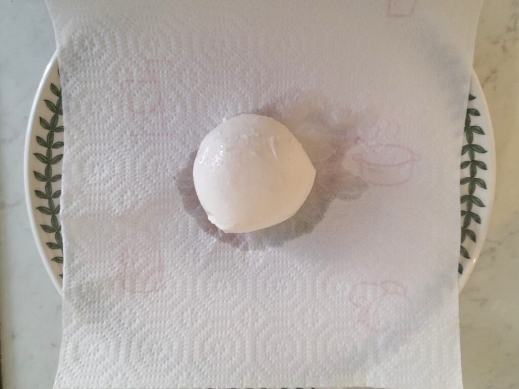 키친타월 위에 올려 물기를 빼는 생모짜렐라 1개가 접시에 놓여 있다