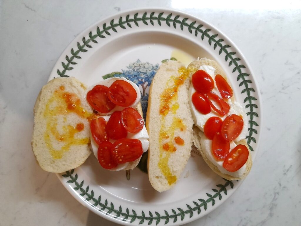 접시 위에 방울토마토와 모짜렐라 치즈 그리고 올리브유를 뿌린 파니노 두개가 있다