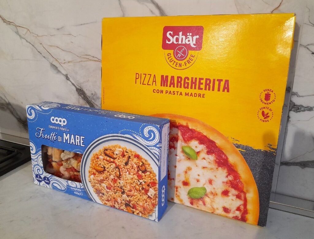 주방 조리대 위에 Schär 글루텐프리 마르게리타 피자와 Coop Frutti di Mare 해산물 제품 상자가 놓여 있다