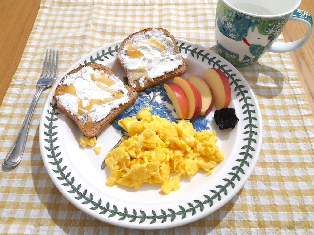 스크램블에그와 리코타를 바른 토스트, 사과 조각, 우유가 한 접시에 놓인 아침 식사