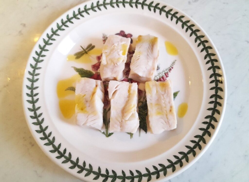 접시에 담긴 흰살생선 위에 올리브유를 뿌린 모습