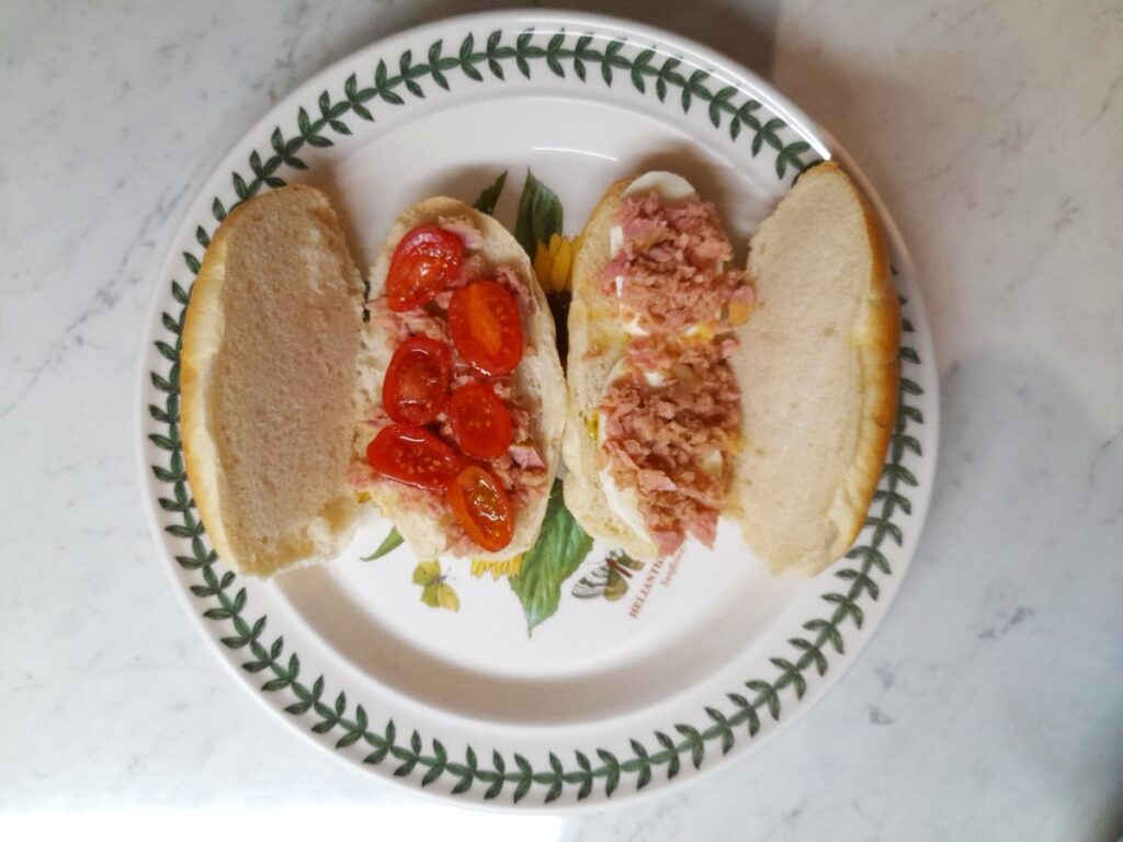 접시위에 각각 속재료가 방울토마토, 참치,올리브유와 모짜렐라치즈, 참치, 올리브유인 파니노 두개가 있다